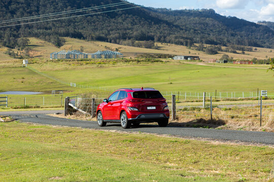 Red electric vehicle car driving down rural country road on sunlit day