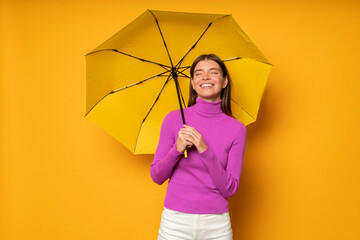 Woman walking under rain with yellow umbrella enjoying fresh air, standing with closed eyes