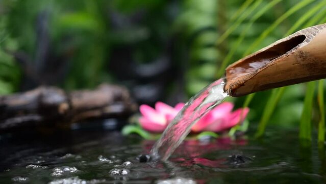 Water flows from bamboo gutter pipes, smoke floats in, pink lotus flowers, blurred green leaf background.