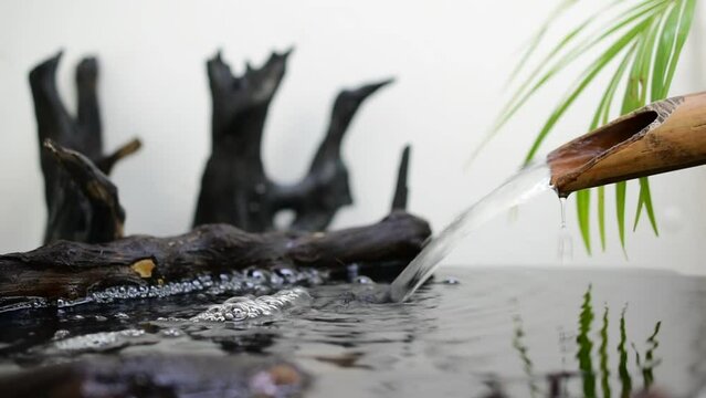 Flowing water, bamboo gutter pipes with black tree stumps, spa treatment concept.