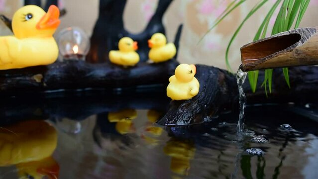 Water flows, pipes, bamboo gutter, mother family and yellow rubber ducklings on a black stump.