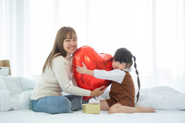 Mother day concept : Happy loving family. Asian mother and her daughter child girl playing in bedroom. holding heart balloon together.