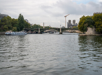 Fototapeta premium Looking West on the River Seine with the Pont Sully and scaffolding shrouded Notre Dame in the distance, Paris, France, repairs, church, cathedral, scaffolding, crane, towers, sully, bridge, pont sull