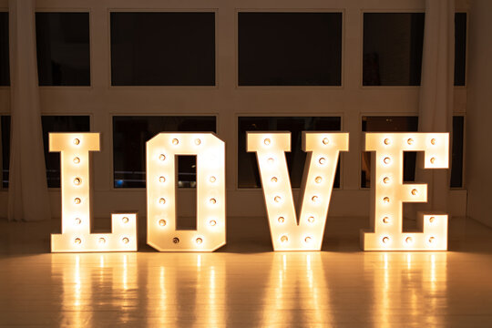 Love big white letters with led retro bulbs glowing. Word LOVE with a big letters. Inscription is love. Glowing large letters. Wedding decor. Illuminated Love sign in large letters near window.	