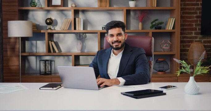 Portrait of Satisfied Young Man working with Laptop and smiling at the camera. Small business owner, company leader or sales manager, male hispanic ceo.