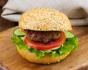 Fresh delicious burger with green salad, lettuce, tomato, cucumber, succulent beef, cheddar on a...