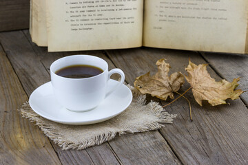 White cup of coffee with autumn leaves and old book on wooden background