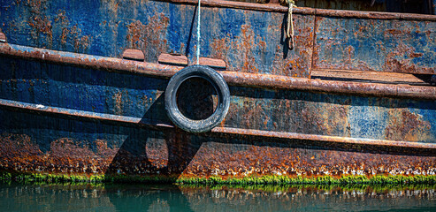 Tyre hanging on the side of a rusty fishing boat for protection.