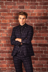 Fototapeta na wymiar Confident young businessman entrepreneur looking at camera at brick wall background. Caucasian male adult in studio. Stylish handsome man model in suit indoors. Fashion style concept. Copy space