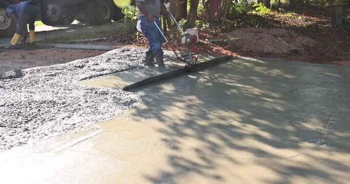 In construction new driveway, machine is used to align on compacted layer fresh concrete