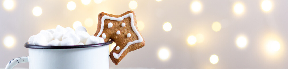 banner of a white cup of winter hot drink with marshmallows and gingerbread star on a white wooden background with bokeh.