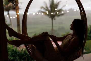 Woman in a rattan chair in a bamboo house enjoys a tropical holiday in Bali. Relax on the outdoor...