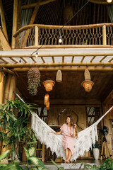 Young pretty woman sit on hammock on balcony of a bamboo eco house in the jungle. Eco tourism.