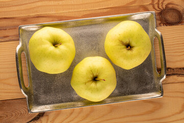 Three ripe yellow apples with a metal tray on a wooden table, macro, top view.