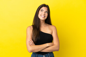 Obraz premium Young Brazilian woman isolated on yellow background looking up while smiling