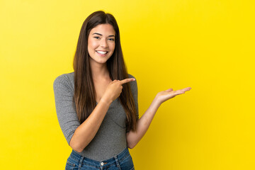 Young Brazilian woman isolated on yellow background holding copyspace imaginary on the palm to...