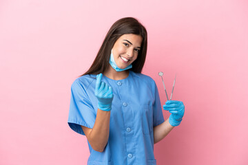 Dentist woman holding tools isolated on pink background making money gesture