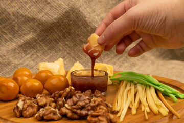 Someone dips a piece of cheese in honey against a background of assorted different varieties of cheese.