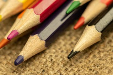 Several colored pencils of different colors on a background of coarse burlap. Close-up, selective focus.