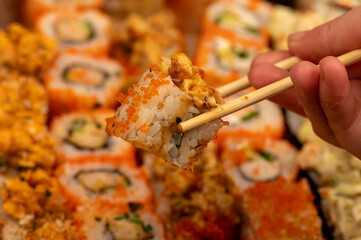 Someone takes a chopsticks roll from a set of different types of rolls in a box.