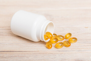 Omega-3 capsules lie in white bottle on a table background. Fish oil tablets top view. Biologically...