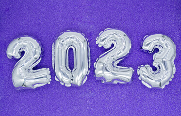 Inflatable shiny silver numbers of the New year 2023 on purple, very peri color background. Copy...