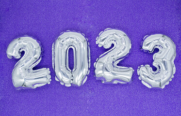 Inflatable shiny silver numbers of the New year 2023 on purple, very peri color background. Copy space