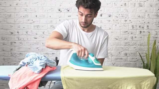 Tired man ironing clothes and feeling bad after exhausting ironing. Household concept