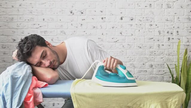 Tired man sleeping while ironing clothes at home. Household concept