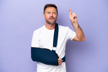 Middle age caucasian man with broken arm and wearing a sling isolated on purple background with...