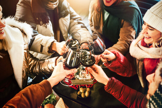 Happy friends group wearing winter clothes celebrating with red wine glasses at patio restaurant table - Young people socializing drinking and eating food sitting outside at winery bar table