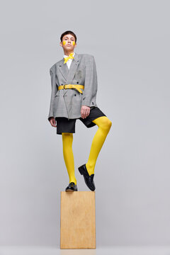 Portrait of stylish boy posing in jacket, blazer and yellow tights and bow isolated over grey background. Statue style