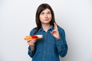 Young Russian woman holding sashimi isolated on white background with fingers crossing and wishing the best