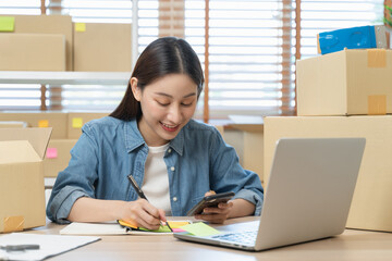 Young Asian woman owner of small online store packing customer orders in the home office.
