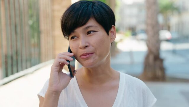 Middle age chinese woman smiling confident talking on the smartphone at street