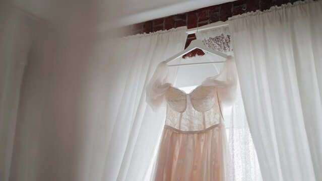 A beautiful pink and white dress hangs in the window span. Very cool light