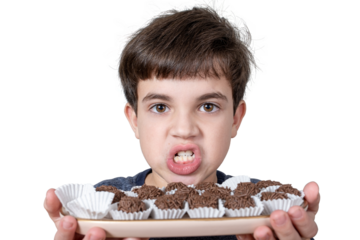 9 year old child holding a tray with several Brazilian fudge balls and grinding his teeth (PNG).