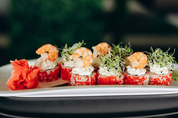 Shrimp sushi on a white plate decorated with caviar, greens and shrimp.