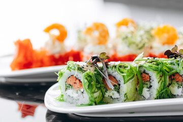 Sushi with smoked salmon on a white plate, decorated with seaweed.