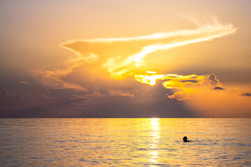 Hollywood Beach in Miami, Florida morning sunrise sun behind sky clouds with reflection path, person people swimming in calm still landscape water