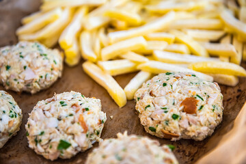 Macro closeup of frozen french chip fries, raw fish crab cakes on baking tray parchment paper for oven before cooking as traditional seafood meal