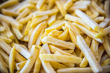 Macro closeup of frozen uncooked raw straight cut salty french fries pommes frites on oven baking tray before cooking or frying with texture detail