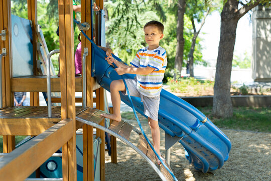 A happy boy climbs a rope up to the playground with slides in the yard.