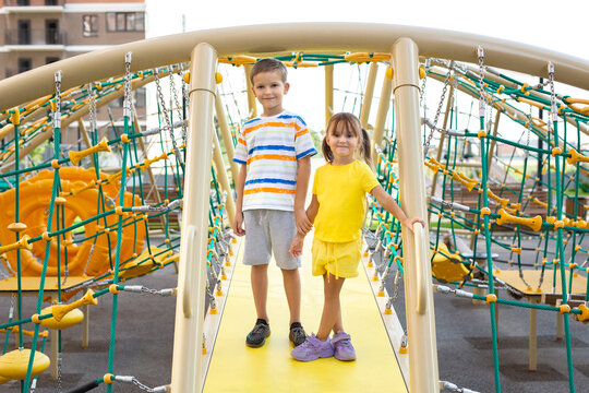 Children, brother and sister, play on a modern playground and climb a giant climbing web.