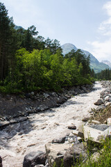 The Baksan mountain river flows in the mountains between the slopes of high cliffs among bright green trees on a clear sunny summer day in Kabardino-Balkaria in the North Caucasus