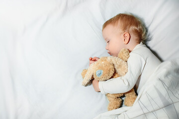 sweet little girl sleeps on white linen in bed. child 1 year old sleeps hugging soft toy. Happy childhood and sleep problems in children concept.