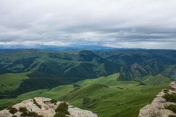 Fototapeta na wymiar Panoramic view of green mountains and hills from the Bermamyt plateau in Karachay-Cherkessia in Russia on a cloudy summer day and copy space in a hazy haze on the horizon
