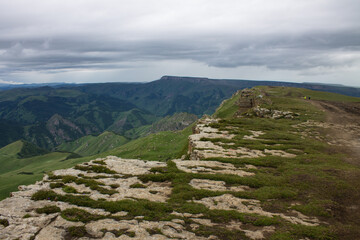 Fototapeta na wymiar Dramatic landscape - panoramic view of the hilly valley from the Bermamyt plateau in Karachay-Cherkessia in a misty haze and stone cliffs
