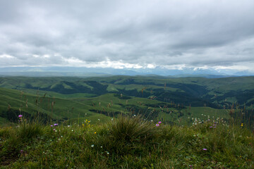 Fototapeta premium Panoramic view of green mountains and hills from the Bermamyt plateau in Karachay-Cherkessia in Russia on a cloudy summer day and copy space in a hazy haze on the horizon
