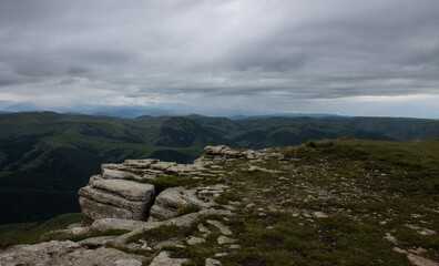 Panoramic view of green mountains and hills from the Bermamyt plateau in Karachay-Cherkessia in Russia on a cloudy summer day and copy space in a hazy haze on the horizon